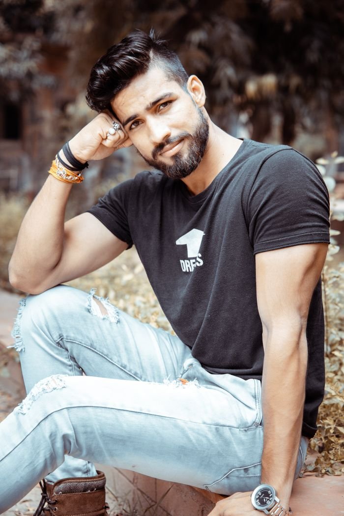 Young man with a beard sitting outdoors, showcasing casual summer fashion.