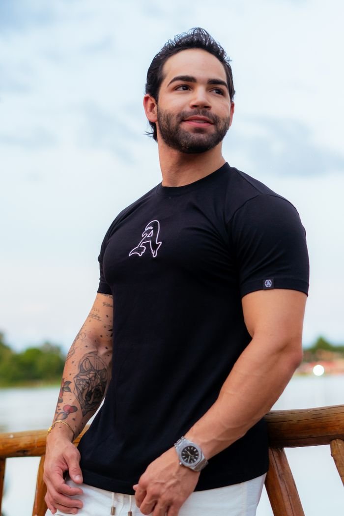 A confident young man in a casual black shirt standing outdoors by a railing during the day.